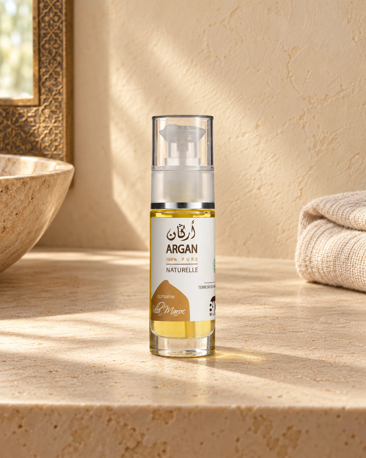 Huile d'Argan 100 % Pure 30ml sur une étagère en pierre claire, avec une serviette en lin, sous une douce lumière naturelle.