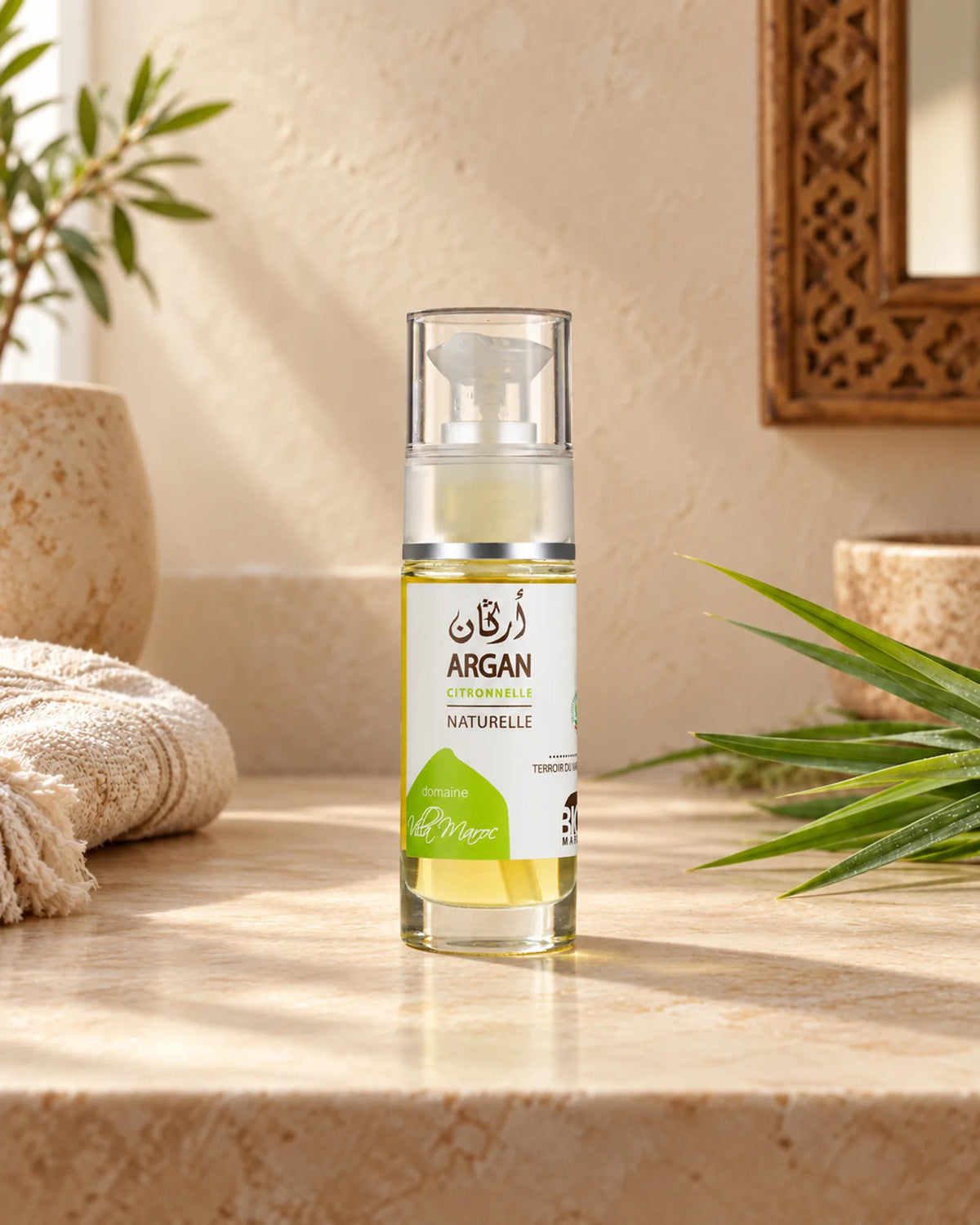 Huile d'Argan à la Citronnelle 30ml sur une étagère en pierre claire, avec un brin de citronnelle, sous une douce lumière naturelle.