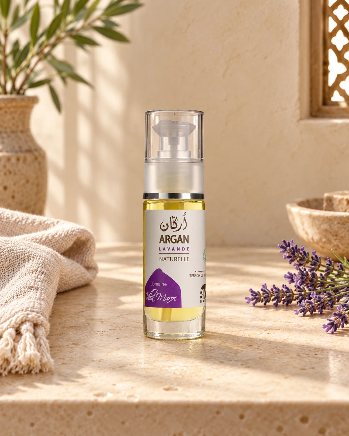 Huile d'Argan Lavande 30 ml sur une étagère en pierre claire, avec un brin de lavande, sous une douce lumière naturelle.