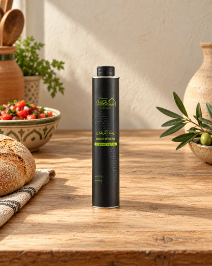 Huile d'Olive Extra Vierge 500ml sur un comptoir en bois, avec du khobz, une salade de tomates et une branche d’olivier.
