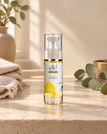 Huile d'Argan et d'Eucalyptus 30 ml sur une étagère en pierre claire, avec une branche d’eucalyptus, sous une douce lumière naturelle.