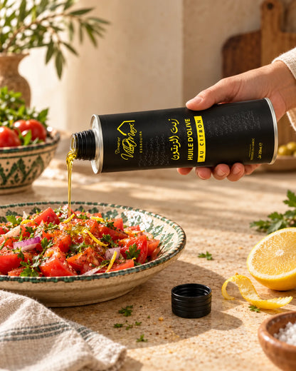 Huile d'Olive au Citron 250ml : une main incline le bidon métallique rigide pour verser un filet d’huile sur une salade de tomates.