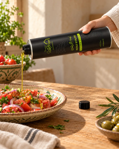 Huile d'Olive Extra Vierge 500ml : une main incline le bidon métallique rigide pour verser un filet d’huile sur une salade de tomates.