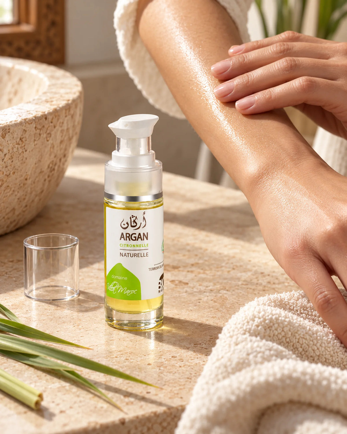 Huile d'Argan à la Citronnelle 30ml sur une vasque en pierre, près de mains qui massent de l’huile sur un avant-bras.