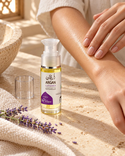 Huile d'Argan Lavande 30 ml sur une vasque en pierre, près de mains qui massent de l’huile sur un avant-bras.